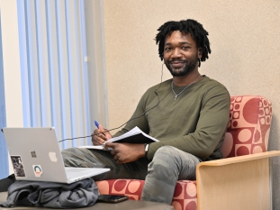 A student sitting on a chair studying while listening to his earphones. 
